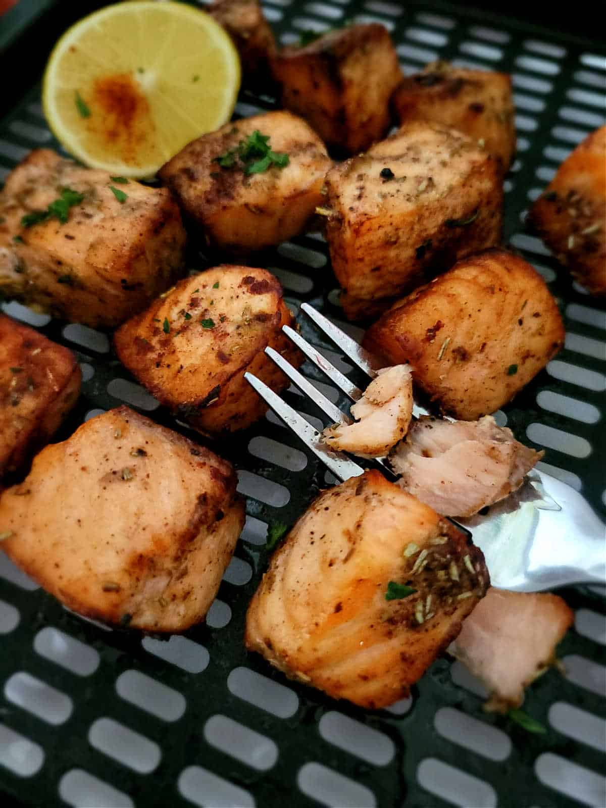 beautifully roasted salmon cubes in air fryer basket with lemon