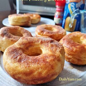 Golden brown air fryer donuts made from Pillsbury biscuit dough, coated in cinnamon sugar and served on a white plate, with a soft and fluffy texture inside.