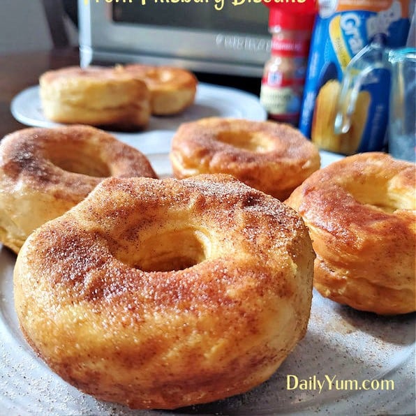 Golden brown air fryer donuts made from Pillsbury biscuit dough, coated in cinnamon sugar and served on a white plate, with a soft and fluffy texture inside.