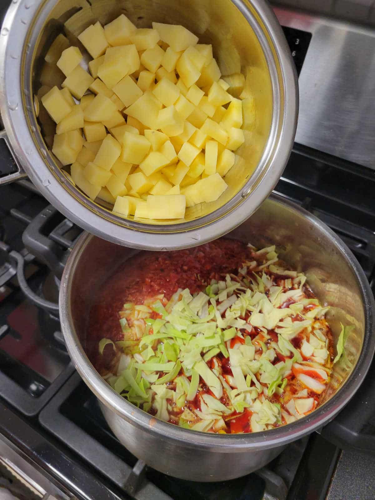 Cubed potatoes being added as the final ingredient to a pot of borscht, ready to cook for 10 minutes until tender.