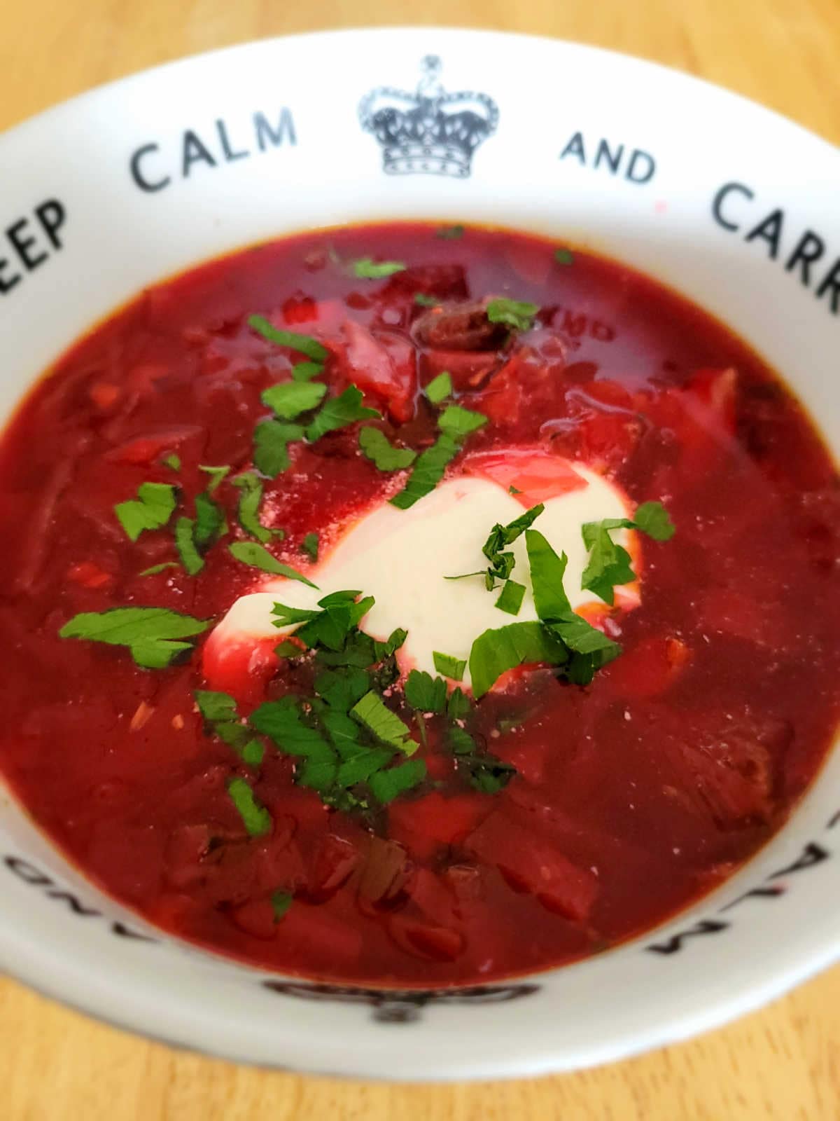 A bowl of hearty borscht soup topped with a dollop of sour cream, garnished with fresh dill, and served with a slice of bread on the side.