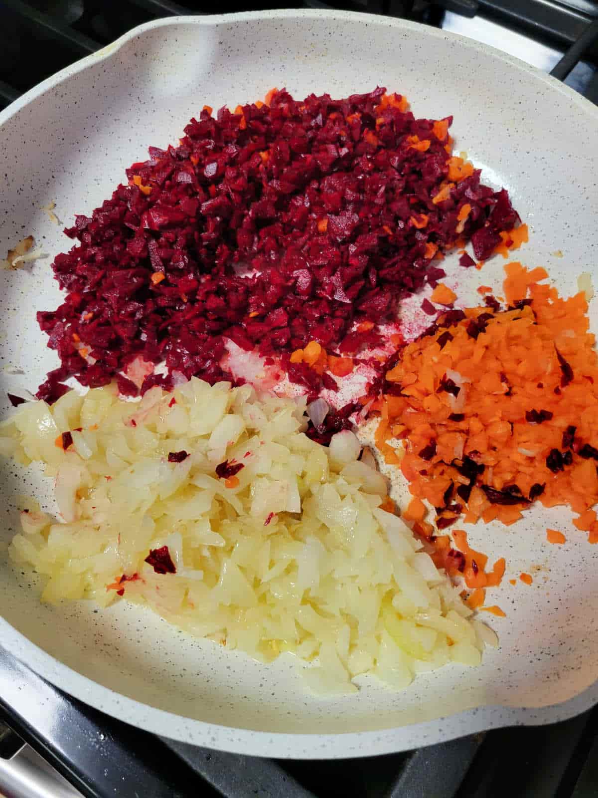 Sautéed onions, carrots, and beets cooking in a pan, with vibrant colors blending together as they soften and caramelize, creating a rich base for borscht.