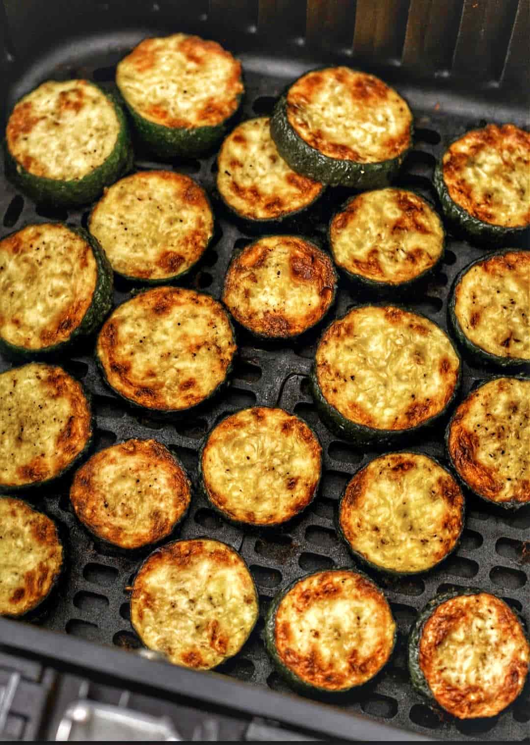 Crispy roasted zucchini slices with charred edges arranged in an air fryer basket